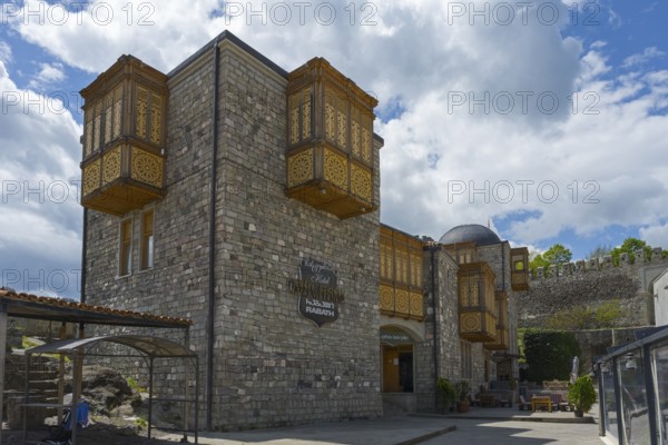 A historic building with intricately decorated wooden balconies against a cloudy sky, Rabati