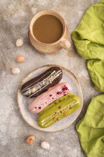 Glazed Eclairs on brown concrete background and green linen textile, cup of coffee, top view, flat