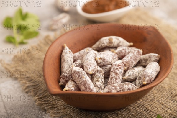 Small smoked Chicken sausages in clay bowl on brown concrete background and linen textile. side