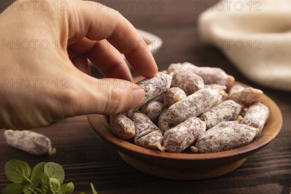 Small smoked Chicken sausages in wooden bowl with hand on brown wooden background and linen textile