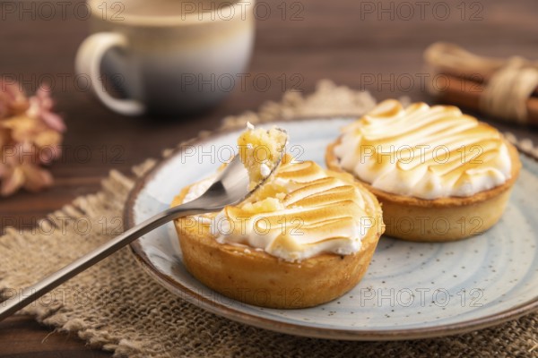French lemon tart with meringue on brown wooden background, cup of coffee, linen textile, side