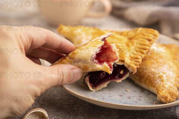 Triangles Pie, Puff Pastry, Samsa with cherry jam on brown concrete background and linen textile