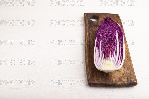 Purple Chinese cabbage on cutting board on white wooden background, side view, copy space,