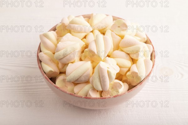 Orange and pink marshmallow in ceramic bowl on white wooden background, side view, copy space,