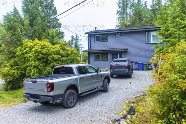 Modern two story gray house featuring a pickup truck and suv parked in a gravel driveway,