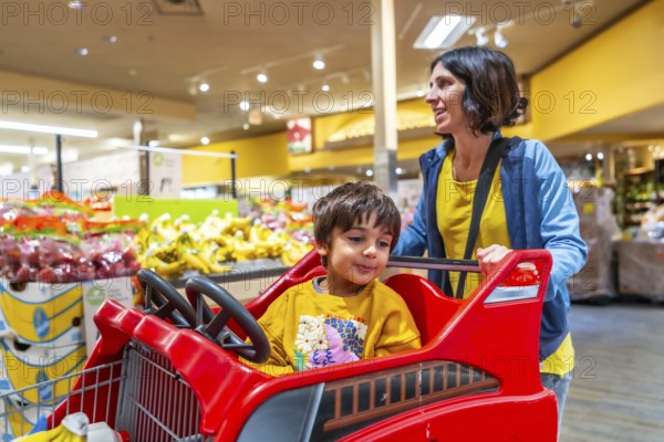 Mother joyfully pushing her son in a specially designed shopping cart resembling a truck during
