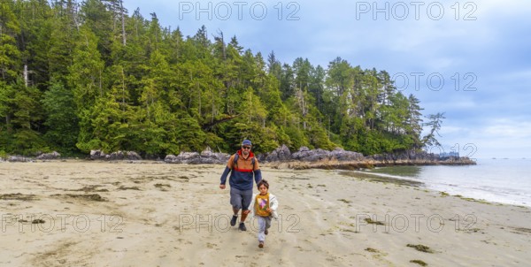 Father and son running together on a sandy beach with lush green forest and rocky coastline in