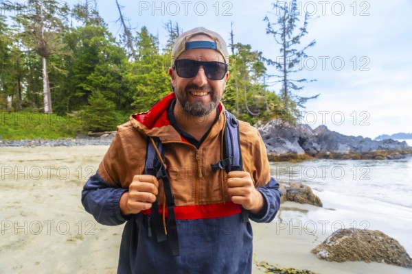 Happy tourist wearing sunglasses and baseball cap is holding his backpack straps while enjoying a