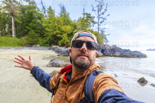 Tourist with sunglasses and baseball cap taking a selfie on chesterman beach, showing the beautiful