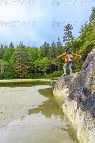 Female hiker standing on rock with open arms, enjoying the serene view of the inlet and lush forest