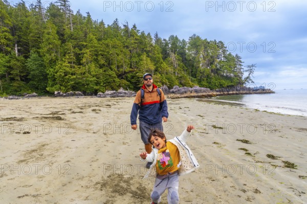 Father and son are walking on chesterman beach in tofino, british columbia, canada, enjoying the