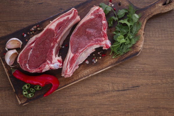 Freshly sliced lamb chops, with herbs and vegetables, on a wooden board, ready to cook, on a wooden
