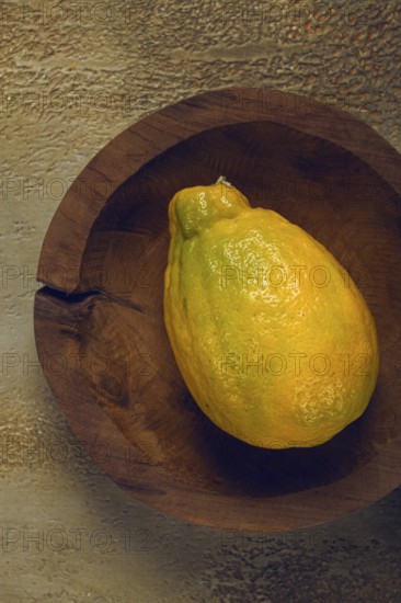 A vibrant yellow fruit, possibly a lemon or a ripe papaya, sits in a handcrafted wooden bowl