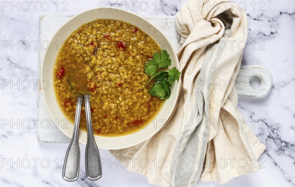 A bowl of delicious lentil soup sits on a marble countertop, garnished with fresh herbs. Silver