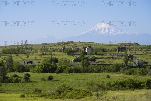 Wide green landscape with views of snow-capped mountains and scattered huts, view of large and