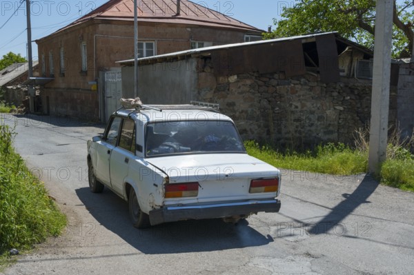 A rear view of an old car on a rural road surrounded by old buildings, Lada 2107, also WAS-2107,