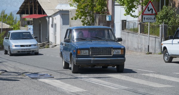 A blue car on a city street surrounded by road signs on a sunny day, Lada 2107, also WAS-2107,