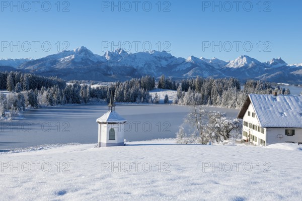 Snowy landscape with chapel, farm and mountains in the background under clear sky, Hegratsrieder