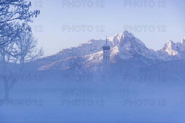 Snowy mountain landscape with St. Coloman pilgrimage church in the foreground and foggy background,