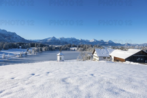 A winter landscape with farm and chapel in front of snowy mountains under a blue sky, Hegratsrieder