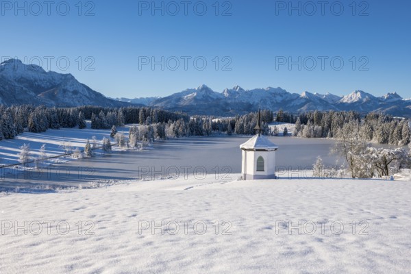 Snow-covered plain with a chapel and mountains under bright blue sky, Hegratsrieder See, near
