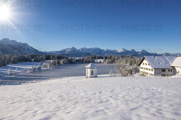 Snowy landscape with chapel, farmhouse and mountains under brilliant sunshine, Hegratsrieder See,