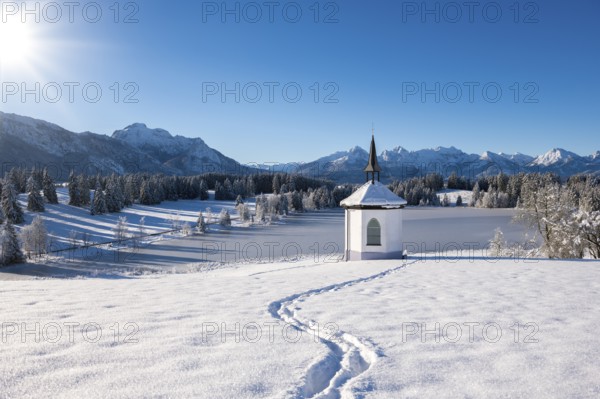 Chapel in snow with footprints and sunny mountain landscape, Hegratsrieder See, near Füssen,