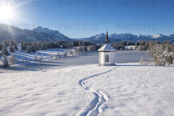 Snowy landscape with chapel and footprints, surrounded by mountains and forests, Hegratsrieder See,