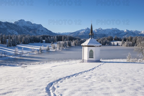 Snowy landscape with chapel and footprints against a mountain backdrop, Hegratsrieder See, near