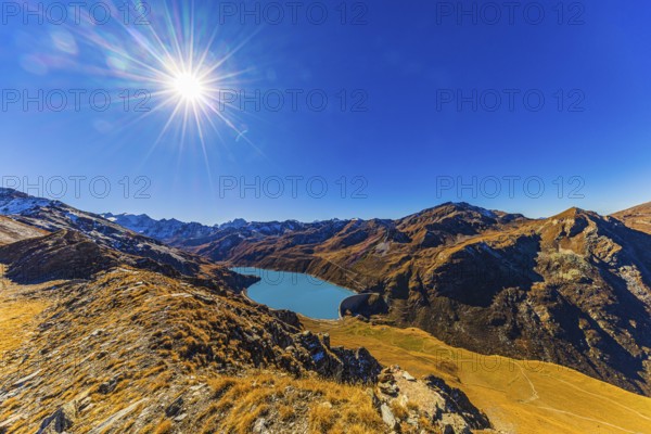 The sun shines over the mountains of the Val d'Anniviers, below the dam and the turquoise Lac de