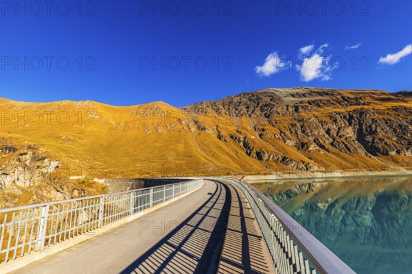 The dam of the Lac de Moiry reservoir, behind alpine meadows in autumn colors, Val d'Anniviers,