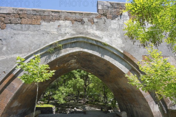 View of an old stone bridge structure against a wooded background on a sunny day, part of a