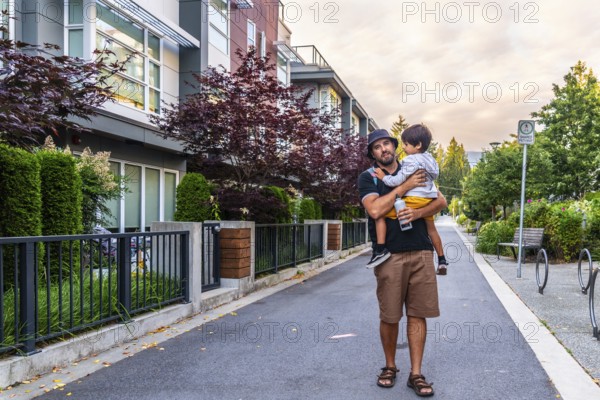 Father carrying his son while walking on a sidewalk in a residential area of vancouver, british