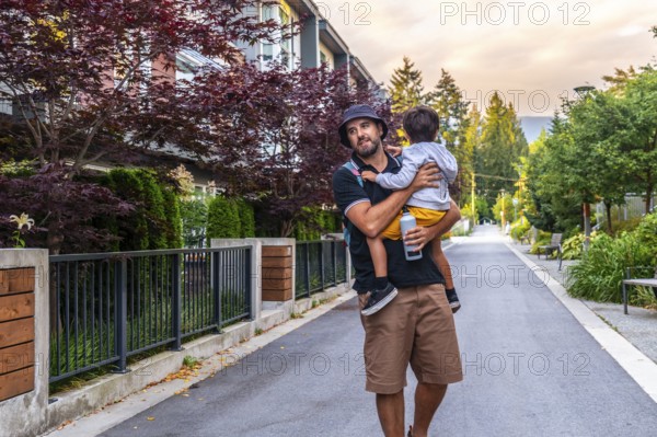 Father carrying his son is walking down a residential street in vancouver, british columbia,