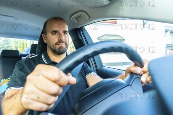 Bearded man driving a modern car in kamloops, british columbia, with a child visible in the back