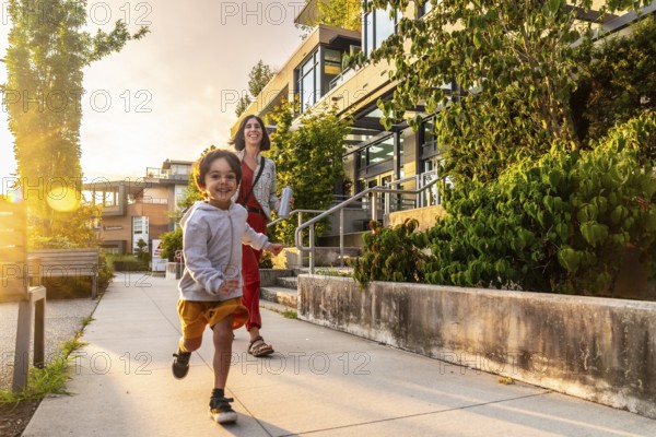 Happy child running joyfully on the sidewalk in vancouver, british columbia, canada, with mother