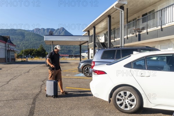 Male tourist wearing headphones and carrying a backpack strolls through a parking lot, pulling a