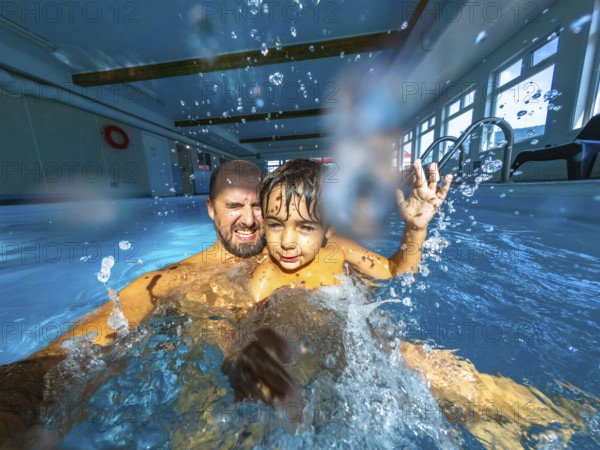 Father and son are having fun in an indoor pool, splashing and playing together, creating a moment