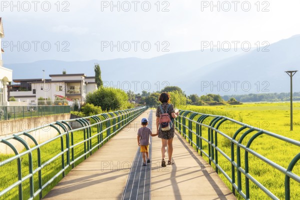 Mother and son enjoying a leisurely stroll on a pedestrian bridge, surrounded by lush greenery and