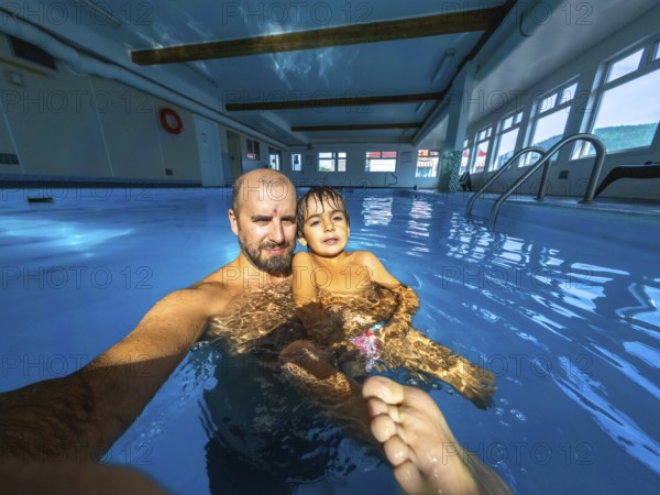 Father and son are taking a selfie while having fun and enjoying time together in a swimming pool