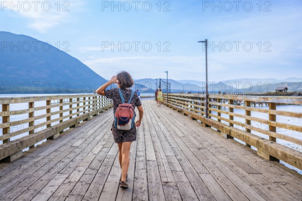 Young woman with backpack walking down a long wooden pier, enjoying the scenic view of the shuswap