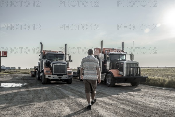 Trucker walking towards two semi trucks parked on a gravel road near hemlock grove boardwalk in the