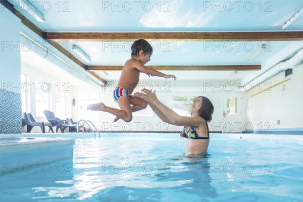 Smiling young mother catching her cheerful son as he leaps joyfully into the indoor swimming pool,