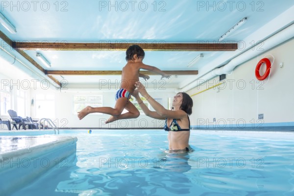Smiling mother catching her joyful son mid air as he jumps into the pool, enjoying a playful moment