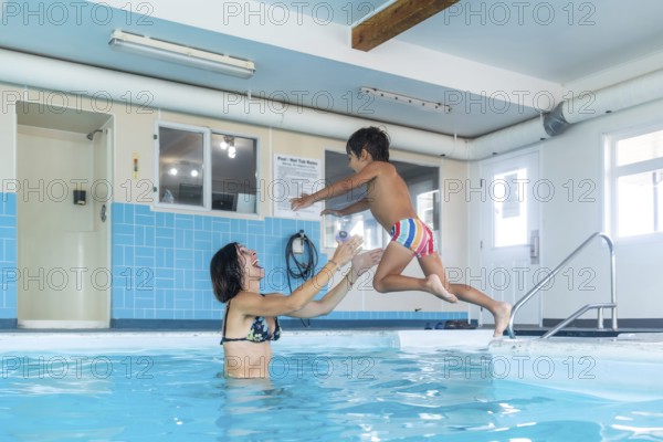 Happy mother catching her smiling son mid jump into a swimming pool at a lively public indoor