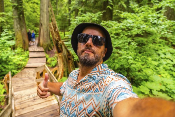 Happy tourist wearing sunglasses and bucket hat taking a selfie while hiking the beautiful giant