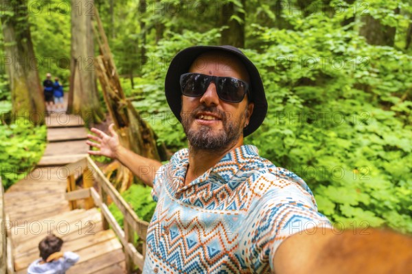 Happy tourist wearing sunglasses and a bucket hat taking a selfie while walking the giant cedars
