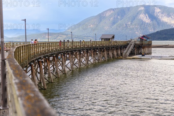 Tourists are walking on the long wooden pier that curves across the shuswap lake in salmon arm,