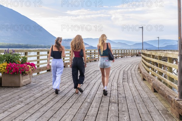 Three young women are enjoying a leisurely stroll along a wooden pier in salmon arm, british