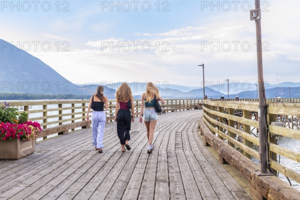 Three young women are enjoying a leisurely stroll along a scenic wooden pier in salmon arm, british